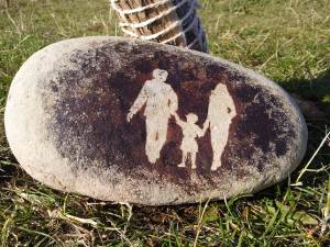 Family group depicted on beach pebble in stencilled cave painting style.